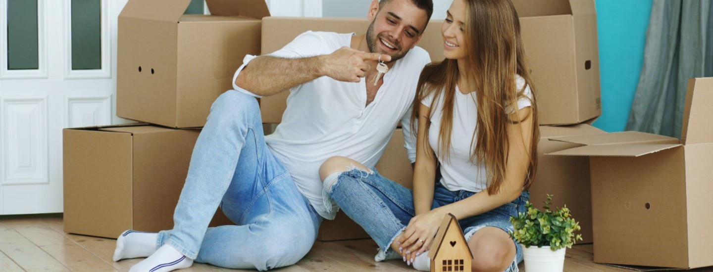 happy first time buyer couple seating down house keys moving boxes